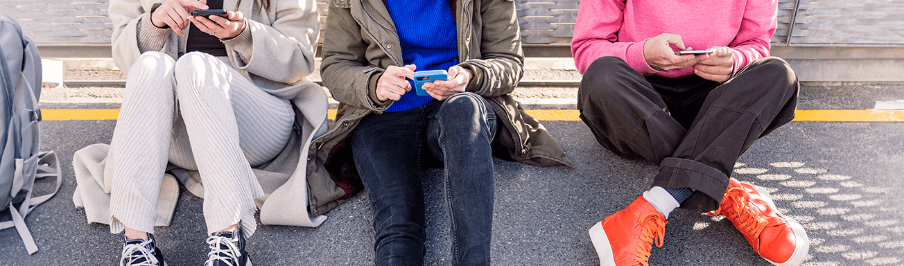 teens sitting side by side scrolling on smartphones