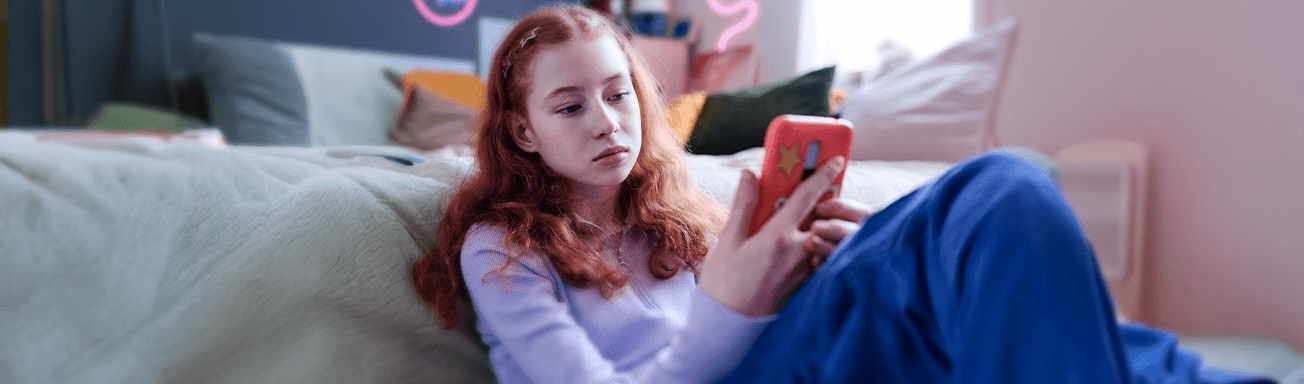 young teen scrolling phone alone in bedroom looking sad
