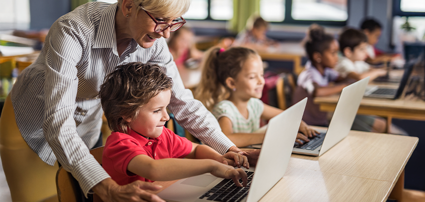 teacher helping young child at school use laptop