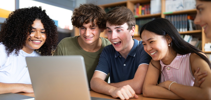 group of happy teenagers on laptop in library setting talking to someone via video chat
