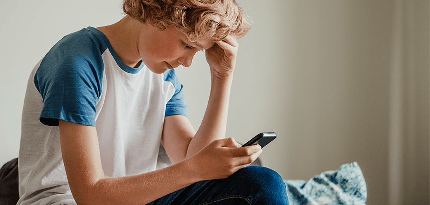 young boy looking down at phone with upset expression on his face