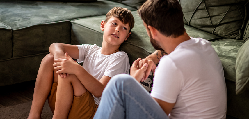 father talks with son holding his cell phone by the couch 
